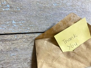 Yellow paper with written message Thank You on brown envelope.
