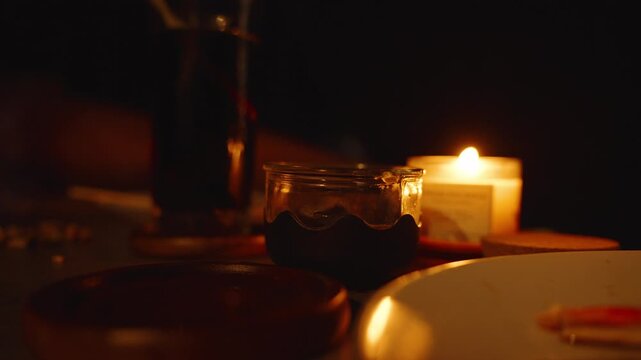 Hand Holding Tall Glass of Dark Drink With Candle Glowing Nearby and Plate With Food Pieces on Table close up Cozy TV Time Concept