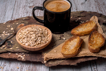 Rustic breakfast scene with a cup of coffee, toasted bread slices, and rolled oats on wooden background. Cozy and warm food styling in natural light