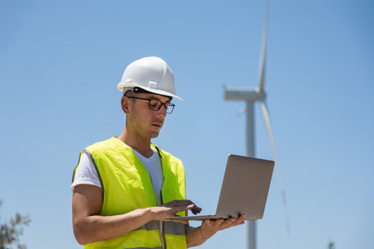 Engineer inspecting wind turbines with laptop outdoors