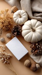 Fototapeta premium A blank white card lies on a refined table alongside dried flowers, pumpkins, and pine cones, creating a seasonal atmosphere