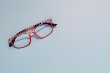 Stylish pink-framed eyeglasses with black arms rest diagonally on a smooth, muted light blue. Ideal...