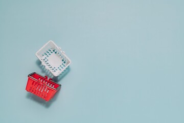 Red and white miniature shopping baskets on light blue. Perfect for themes of retail, consumerism, and online shopping.