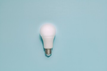 Single white LED light bulb stands upright on smooth, muted blue. Symbolizes ideas, innovation, energy efficiency, and sustainable technology.