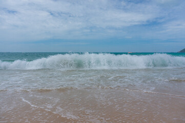 Seascape on waves with foam and spray, sky and beach. Ocean waves crashing on a sandy beach