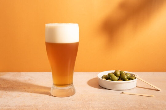 Glass of beer with olives on a warm orange background