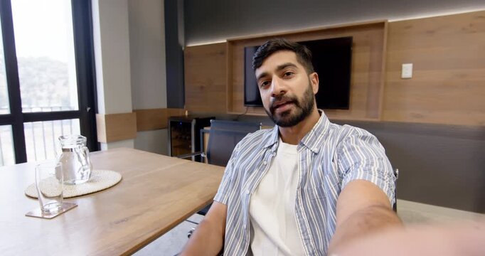 Taking selfie Indian man sitting at conference table in hotel suite, with water pitcher, copy space