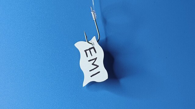 EMI word written on a paper and hooked on a fishing hook like lure. Isolated with blue background. loan repay, debt accumulation, payment crisis, liability, finance burden and payout struggle concept.