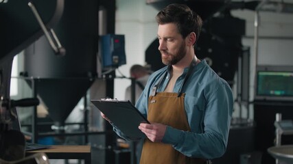 Caucasian man barista small business owner coffee roasting machine control check inspection production factory male guy writing notes roaster quality checklist thoughtful inspector manufacture worker