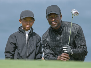 African American man and boy in matching golf attire, posing together on a golf course, showcasing their enthusiasm for the sport and bonding over shared interests