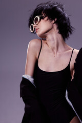 Fototapeta premium young woman in black top wearing oversized sunglasses with short dark hair posing against a neutral background showing stylish modern fashion and attitude