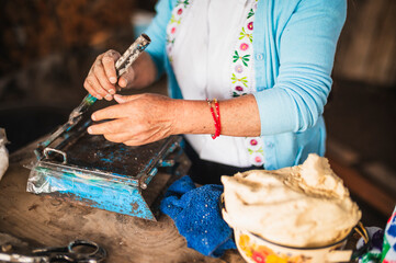 An indigenous Mexican woman wearing a white embroidered blouse and blue sweater, pressing dough...