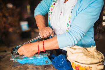 An indigenous Mexican woman wearing a white embroidered blouse and blue sweater, pressing dough into a tortilla press to make tortillas, a traditional Mexican dish.
