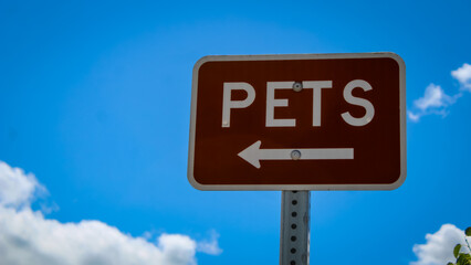 Close-up of a sign indicating the way to a designated pet walking area isolated against a blue sky.