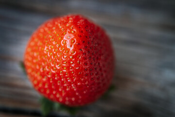 Macro image of a bright red, ripe strawberry lying on a rustic wooden surface, with visible seeds...