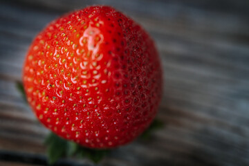 Macro image of a bright red, ripe strawberry lying on a rustic wooden surface, with visible seeds...