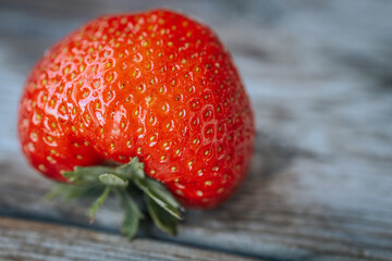 Macro image of a bright red, ripe strawberry lying on a rustic wooden surface, with visible seeds...