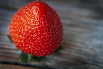 Macro image of a bright red, ripe strawberry lying on a rustic wooden surface, with visible seeds...
