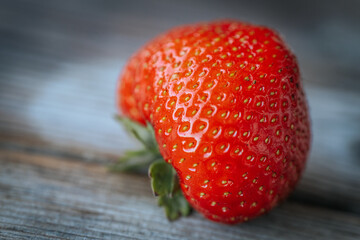 Macro image of a bright red, ripe strawberry lying on a rustic wooden surface, with visible seeds and a shiny, fresh texture.