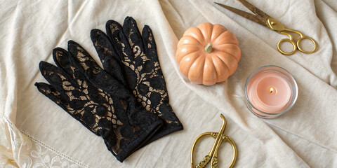 Halloween themed still life featuring black lace gloves, a burning scented candle, a small pumpkin, and golden scissors on a beige linen cloth, creating a cozy atmosphere