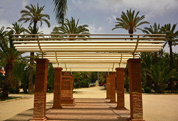 ażurowa pergola w egzotycznym ogrodzie, egzotyczny ogród z drewnianą, falistą pergolą i palmami, wooden pergola amidst tropical greenery, an exotic garden with a wooden, wavy pergola and palm trees © kateej