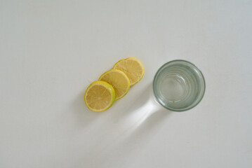 Top view of three lemon slices and an empty glass on white background, minimal composition.