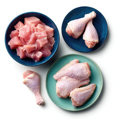 Overhead view of diced chicken in bowl and chicken legs and wings on plates against white background