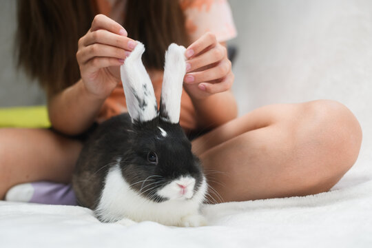 Girl playing with rabbit ears while sitting on bed.