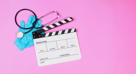 Clapper board with stethoscope and latex glove on pink background.