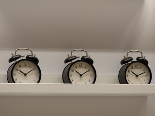 Three Classic Black Twin-Bell Alarm Clocks Aligned on White Shelf