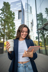Businesswoman walking and using tablet while holding reusable coffee cup in urban setting
