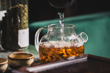 Fototapete Tee Glass teapot with loose leaf tea brewing in hot water, steam rising. Ceramic cups and tea jar on table create a cozy, rustic tea preparation scene  © pavel siamionov