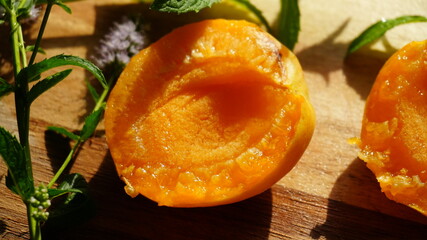 Fresh ripe apricots cut in halves on a wooden surface with mint leaves and natural sunlight. Summer fruit ideal for healthy eating, organic food, or seasonal harvest themes.
