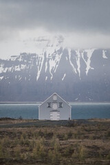 Minimal White House by Icelandic Fjord with Snowy Mountains and Moody Sky