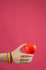 Woman with engagement ring and rainbow bracelet holding heart on pink background. Copy space. 