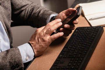 Businessman working at modern office desk, holding smartphone and pen, writing in notebook, with keyboard and mouse on the table.