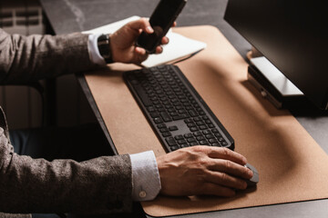 Businessman working at modern office desk, holding smartphone and pen, writing in notebook, with...
