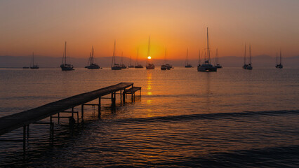 Fototapeta premium Sunset Over Sea with Sailboats and Pier