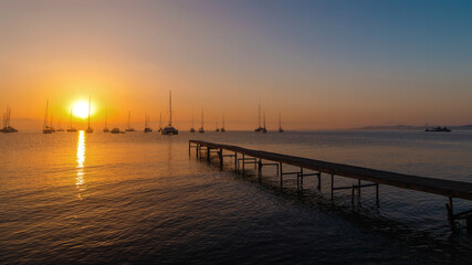 Obraz premium Sunset Over Calm Sea with Sailboats and Pier