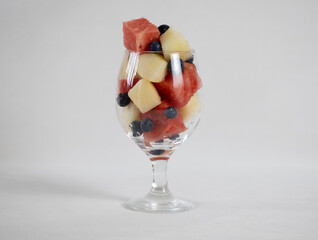 Watermelon and melon cubes, and blueberry in a glass on a light background
