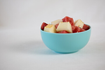Watermelon and melon cubes in a blue bowl on a light background