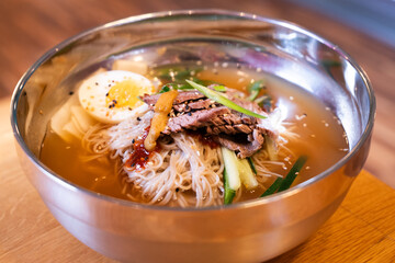 Korean cold beef noodle soup in metal bowl – front view