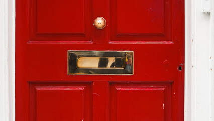 Architectural fragment of English home red door with vintage mail slot and handle