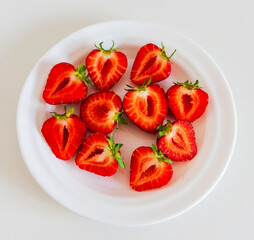 Close-up of bright red strawberry halves with green tops on a round white plate. Fresh fruit snack, clean food concept, high in vitamins, ideal for healthy lifestyle.