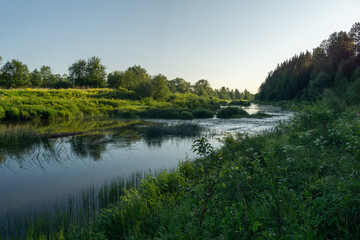 Serene river landscape with lush greenery and calm water reflecting the sky, surrounded by trees...