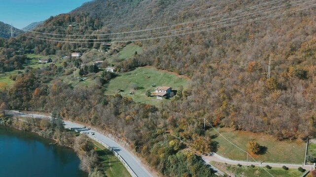 Drone shot of Lake Idro with hillside homes, autumn trees, green meadows, and blue water
