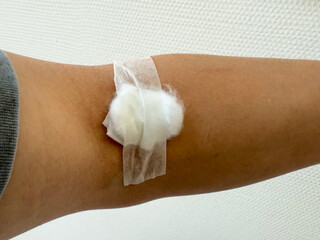 Arm of man has cotton swab to close the wound after blood test. Cotton ball with plaster cover skin...