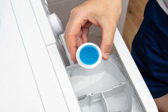 A man pours blue laundry gel or conditioner into a washing machine. Water softener. Washing gel