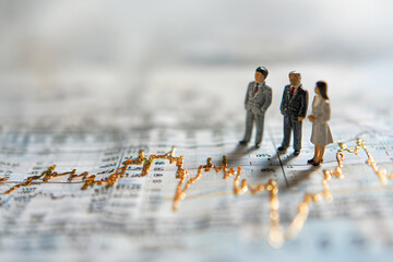 Business professionals analyzing financial trends with miniature figures on stock market charts during trading hours