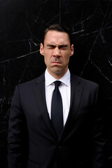 Man in Formal Suit Shows Discomfort in Front of Dark Background During a Business Event